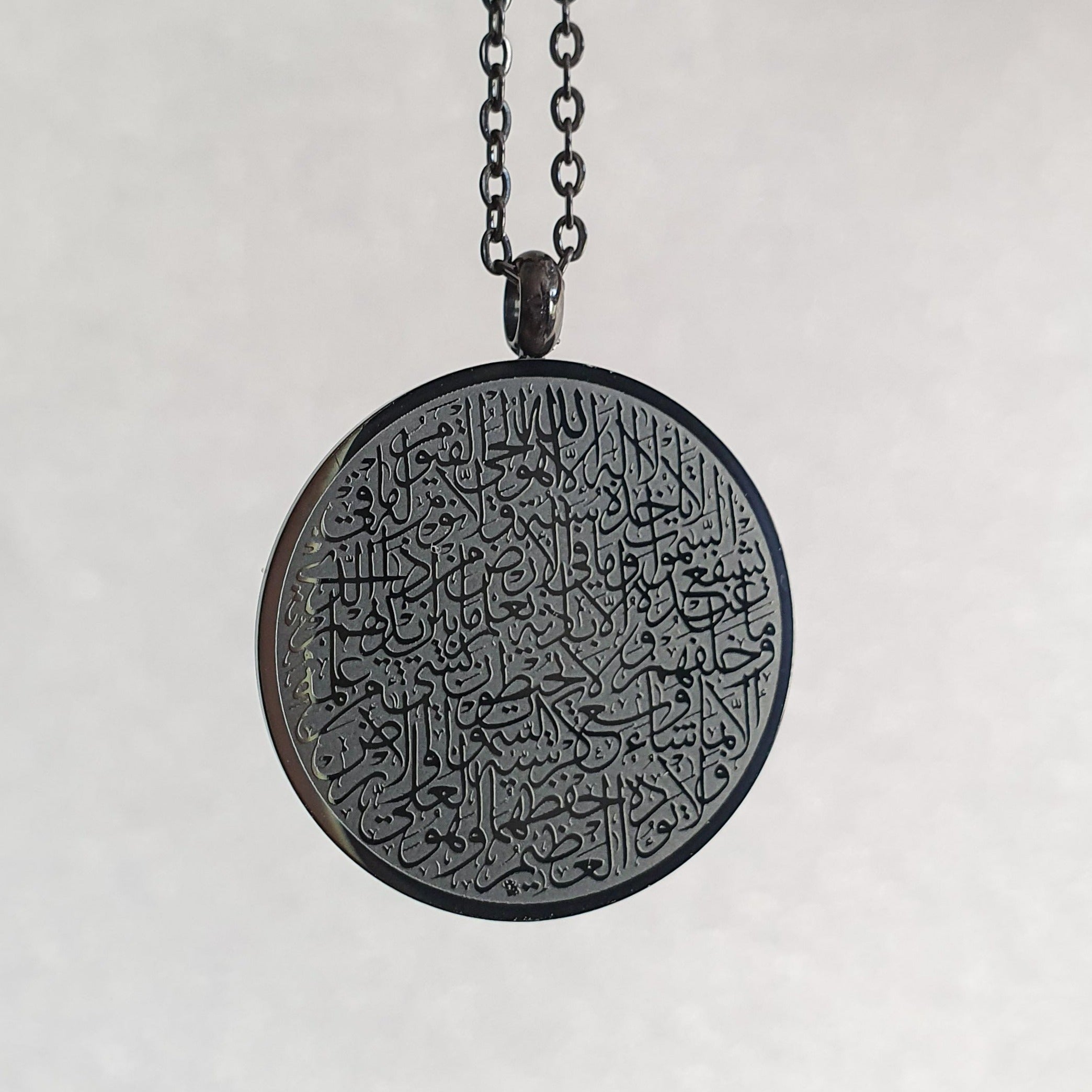 Schwarze Halskette mit rundem Anhänger auf dem in arabischer Schrift und feinster Kalligrafie Ayatul Kursi, der Thronvers eingraviert ist